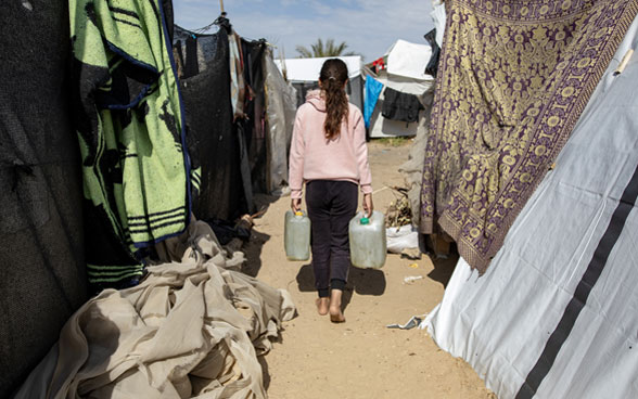 Une fillette palestinienne porte deux conteneurs d'eau dans un camp de tentes pour personnes déplacées à Gaza.